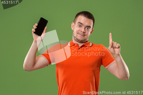 Image of The happy man showing at empty screen of mobile phone against green background.