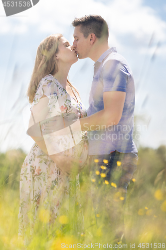 Image of Young happy pregnant couple in love holding hands, relaxing in meadow.