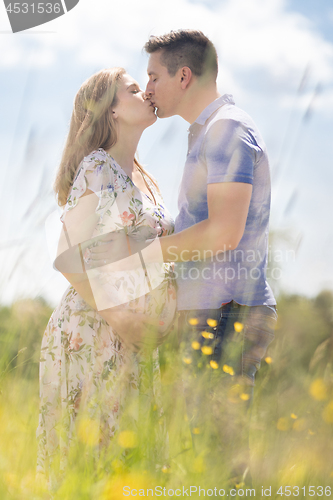 Image of Young happy pregnant couple in love holding hands, relaxing in meadow.