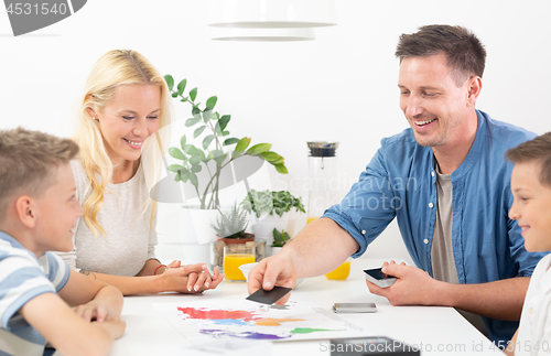 Image of Happy young family playing card game at dining table at bright modern home.