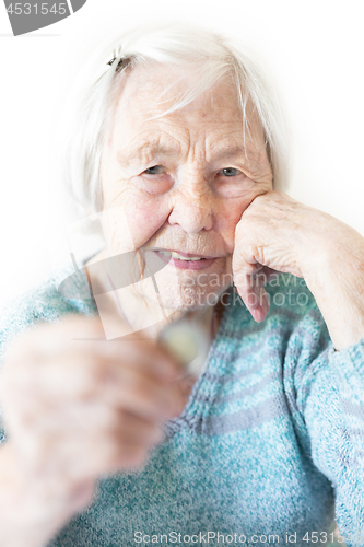 Image of Cheerful elderly 96 years old woman sitting at table at home happy with a coin in her hand. Saving for retirement and financial planing concept