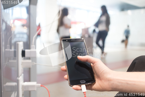 Image of Female hands holding and using smartphone while charging it in a public place using electric plug and a charging cable