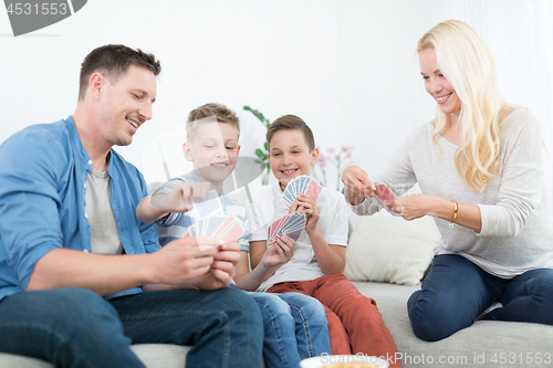 Image of Happy young family playing card game at home.