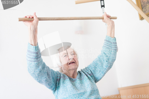 Image of Elderly 96 years old woman exercising with a stick sitting on her bad.