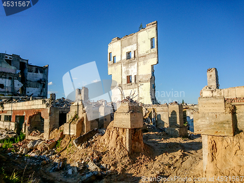 Image of The ruins of a large destroyed building, pieces of stone, concrete, clay and metal against the blue clear sky.