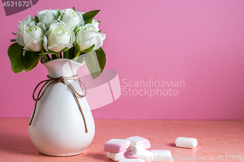 Image of Copyspace with colorful mini marshmallows on a table next to white roses on a pink background.