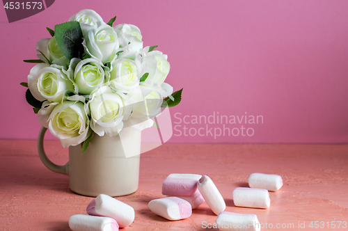 Image of Copyspace with colorful mini marshmallows on a table next to white roses on a pink background.