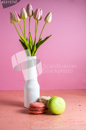 Image of Makaroons on a pink background next to a bouquet of tulips in a white vase and copy space