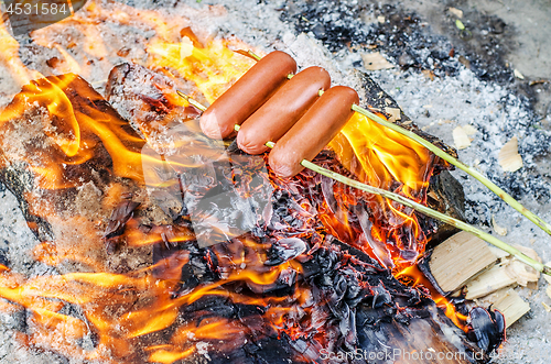 Image of Grilling sausages over an open fire outdoors.