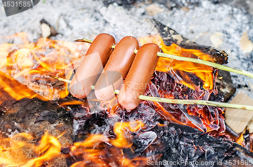 Image of Grilling sausages over an open fire outdoors.