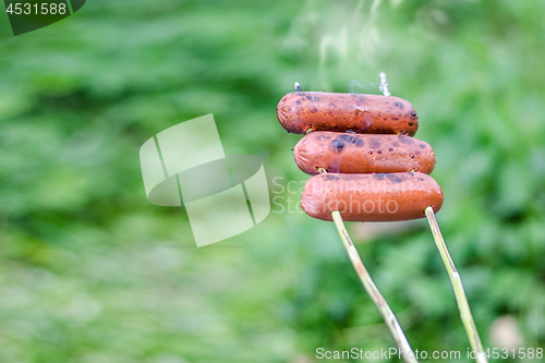 Image of Grilling sausages over an open fire outdoors.