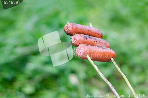 Image of Grilling sausages over an open fire outdoors.