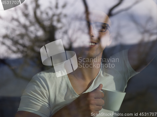 Image of young man drinking morning coffee by the window