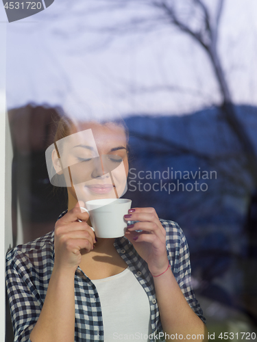 Image of young woman drinking morning coffee by the window