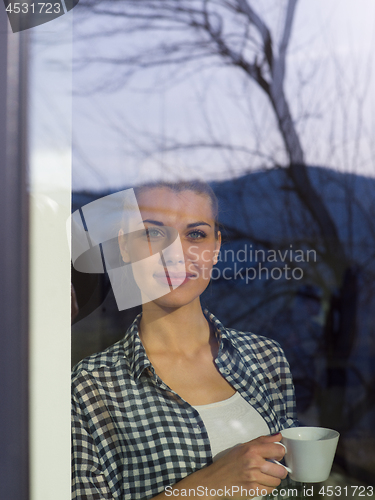 Image of young woman drinking morning coffee by the window