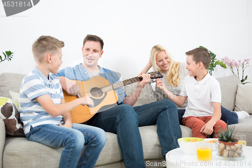 Image of Happy caucasian family smiling, playing guitar and singing songs together at cosy modern home