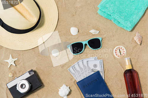 Image of money in passport, shades and hat on beach sand