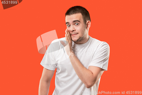 Image of The young man whispering a secret behind her hand over orange background