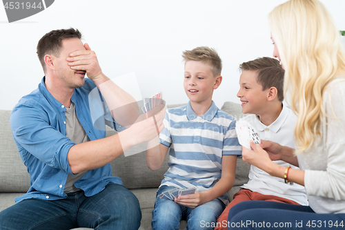 Image of Happy young family playing card game at home.