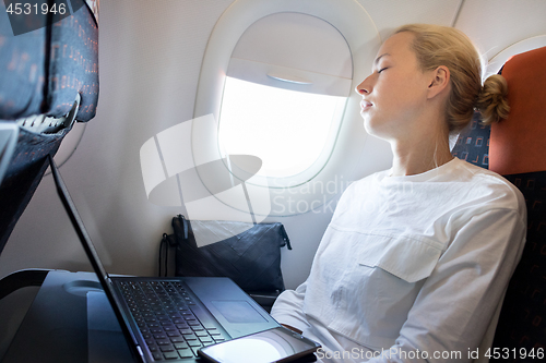 Image of Tired business woman napping on airplane during her business trip woking tasks.