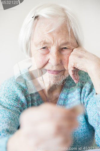 Image of Sad elderly woman sitting at the table at home and looking miserably at only remaining coin from pension in her hand.