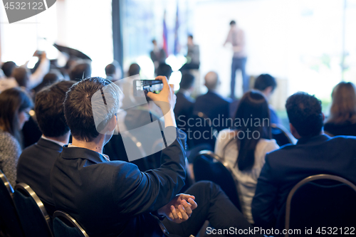 Image of Businessman takes a picture of corporate business presentation at conference hall using smartphone.