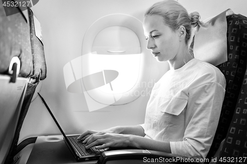 Image of Attractive caucasian female passenger working at modern laptop computer using wireless connection on board of commercial airplane flight