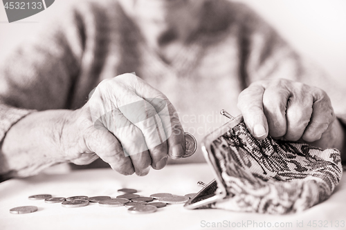 Image of Detailed closeup photo of unrecognizable elderly womans hands counting remaining coins from pension in her wallet after paying bills.