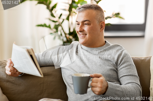 Image of man reading newspaper and drinking coffee at home