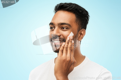 Image of happy indian man applying cream to face