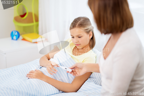 Image of mother giving thermometer to ill daughter at home