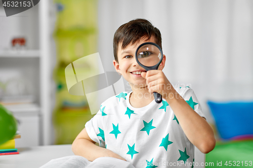 Image of happy boy looking through magnifier at home