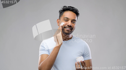 Image of happy indian man applying cream to face