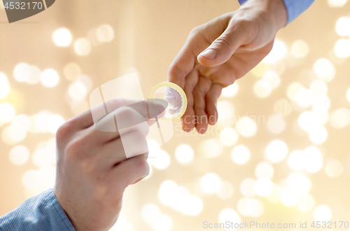 Image of close up of male gay couple hands giving condom