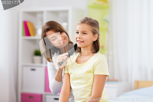 Image of happy mother brushing daughter hair at home