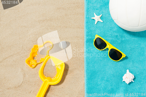 Image of sunglasses, sand toys and ball on beach towel