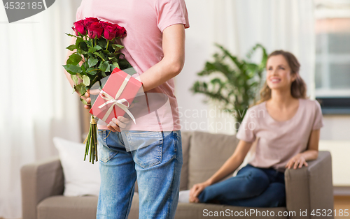 Image of woman looking at man with flowers and gift at home