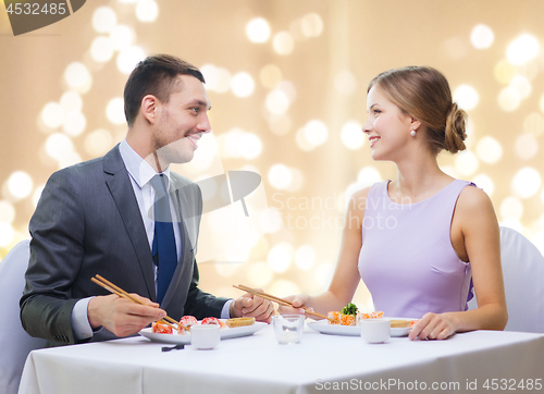 Image of smiling couple eating sushi rolls at restaurant