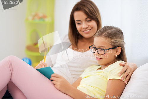 Image of happy girl with mother writing to notebook at home