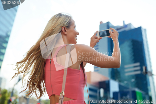 Image of young woman with smartphone photographing city