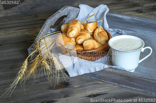 Image of Croissants, a cup with kefir and ears of grain on a wooden tray. The concept of a wholesome breakfast.