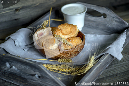 Image of Croissants, a cup with kefir and ears of grain on a wooden tray. The concept of a wholesome breakfast.