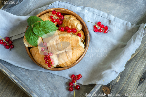 Image of Croissants with currant berries on a wooden tray. The concept of a wholesome breakfast.