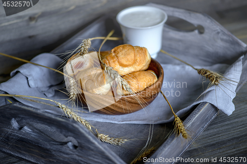 Image of Croissants, a cup with kefir and ears of grain on a wooden tray. The concept of a wholesome breakfast.