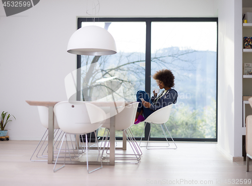 Image of black woman drinking coffee and using a mobile phone  at home