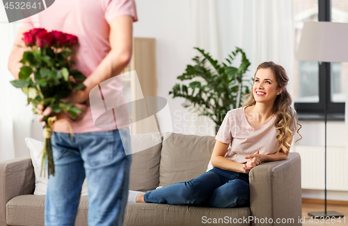 Image of woman looking at man with bunch of flowers at home