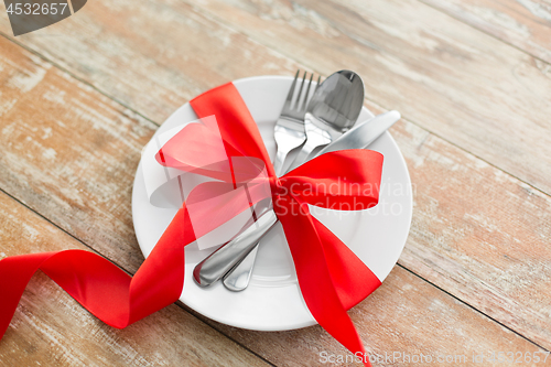 Image of cutlery tied with red ribbon on set of plates