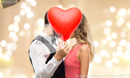 Image of couple hiding behind red heart shaped balloon