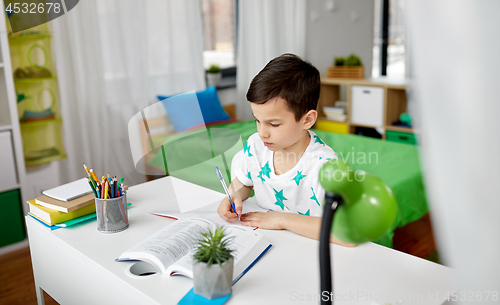 Image of student boy with book writing to notebook at home