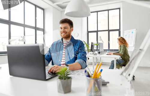 Image of smiling creative man with laptop working at office